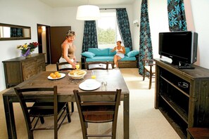 A dining area with a table set for two, a television, and a sofa in the background.