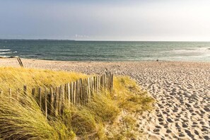 A sandy beach with a wooden fence and grass in the foreground.