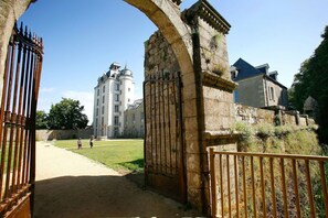 A historic building with a large arched entrance, a pathway leading to a courtyard, and a tall tower.