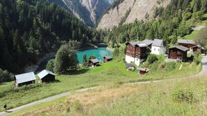 A mountain village with traditional wooden houses, a clear turquoise lake, and a road leading through the valley. - Chalet in Wiler near Ski Lift & Views (Fiesch)