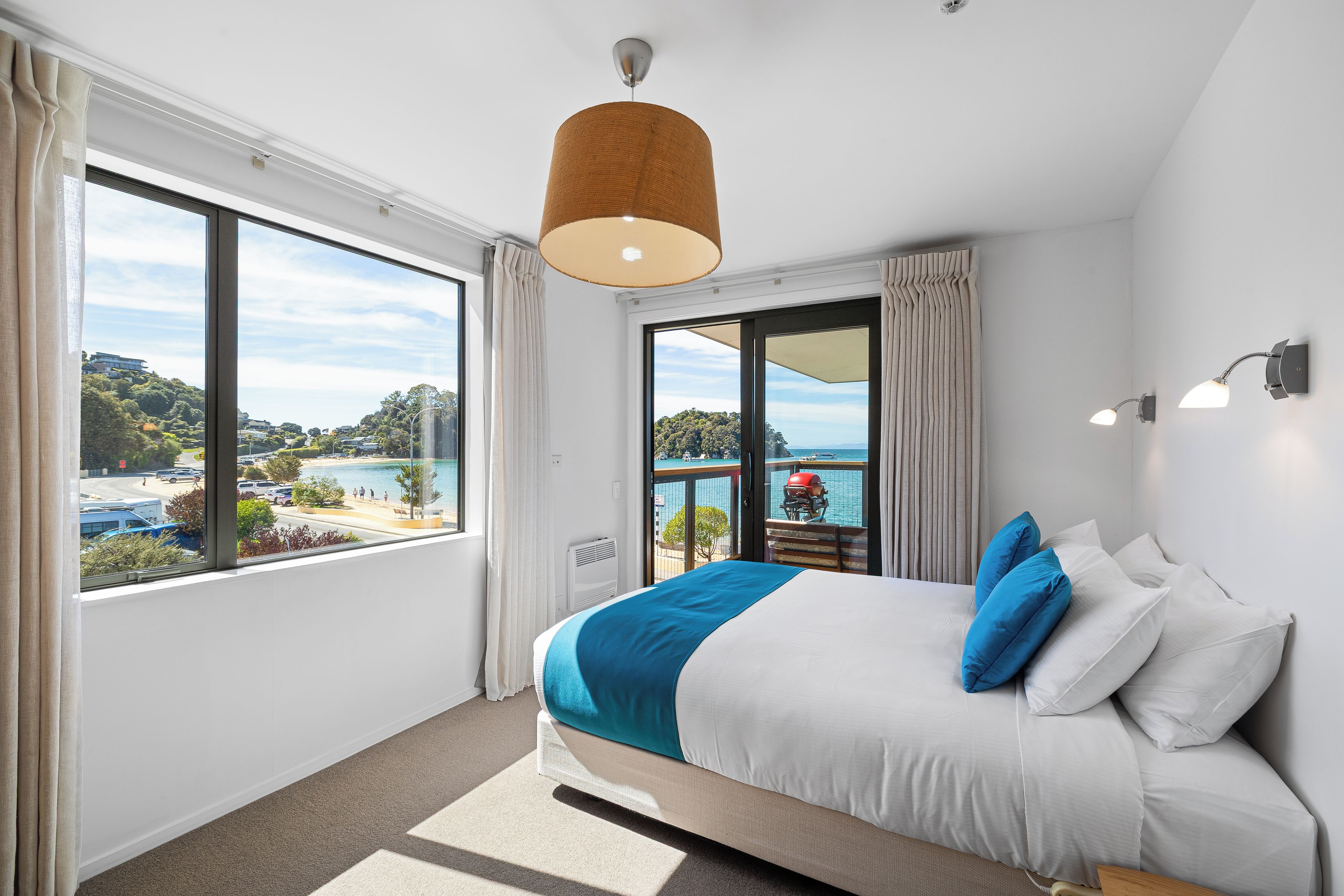 Habitación de hotel con una cama grande, vistas al mar y un balcón con barbacoa.
