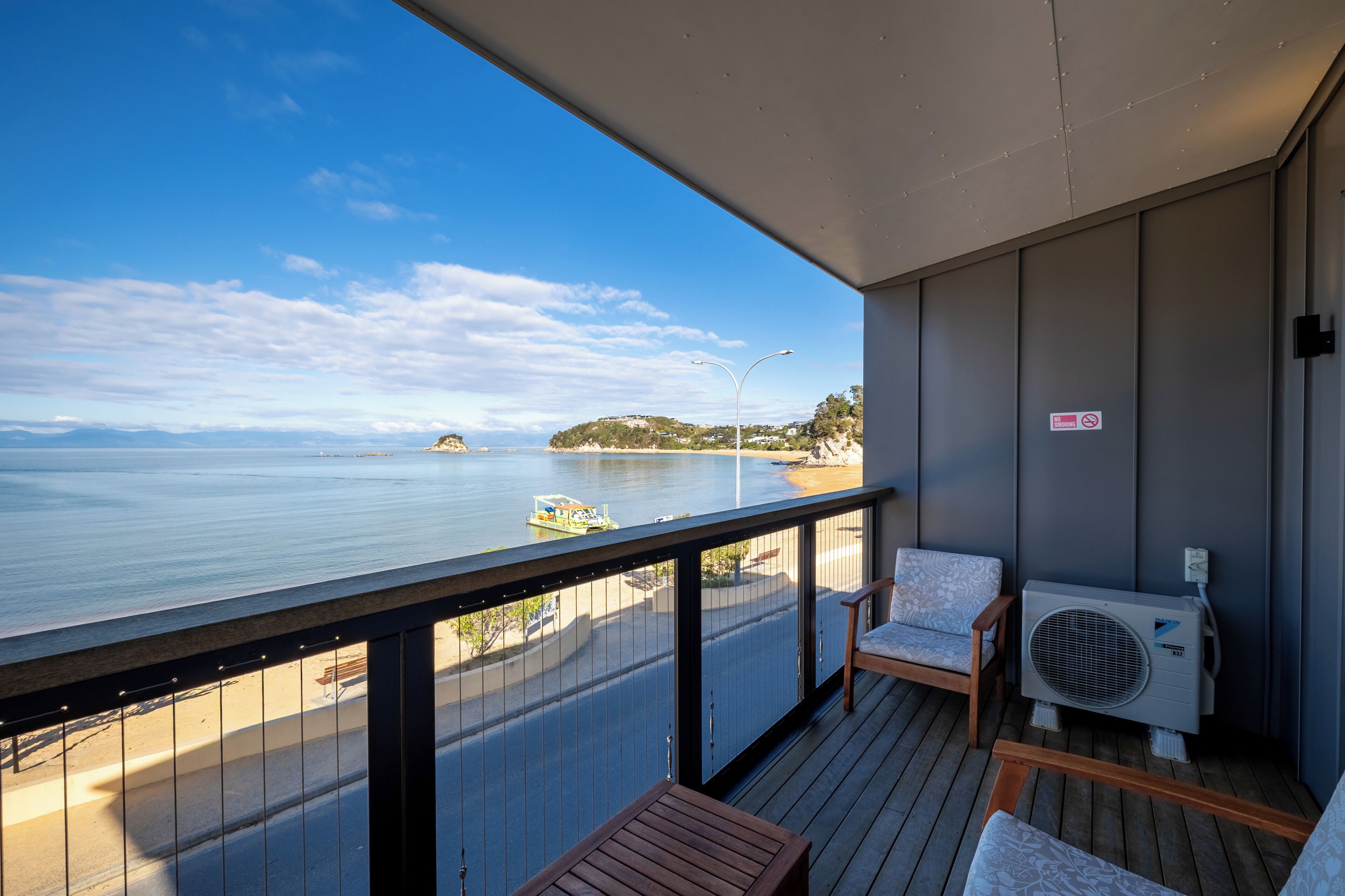 A balcony with a view of the sea, a chair, a table, and an air conditioning unit.