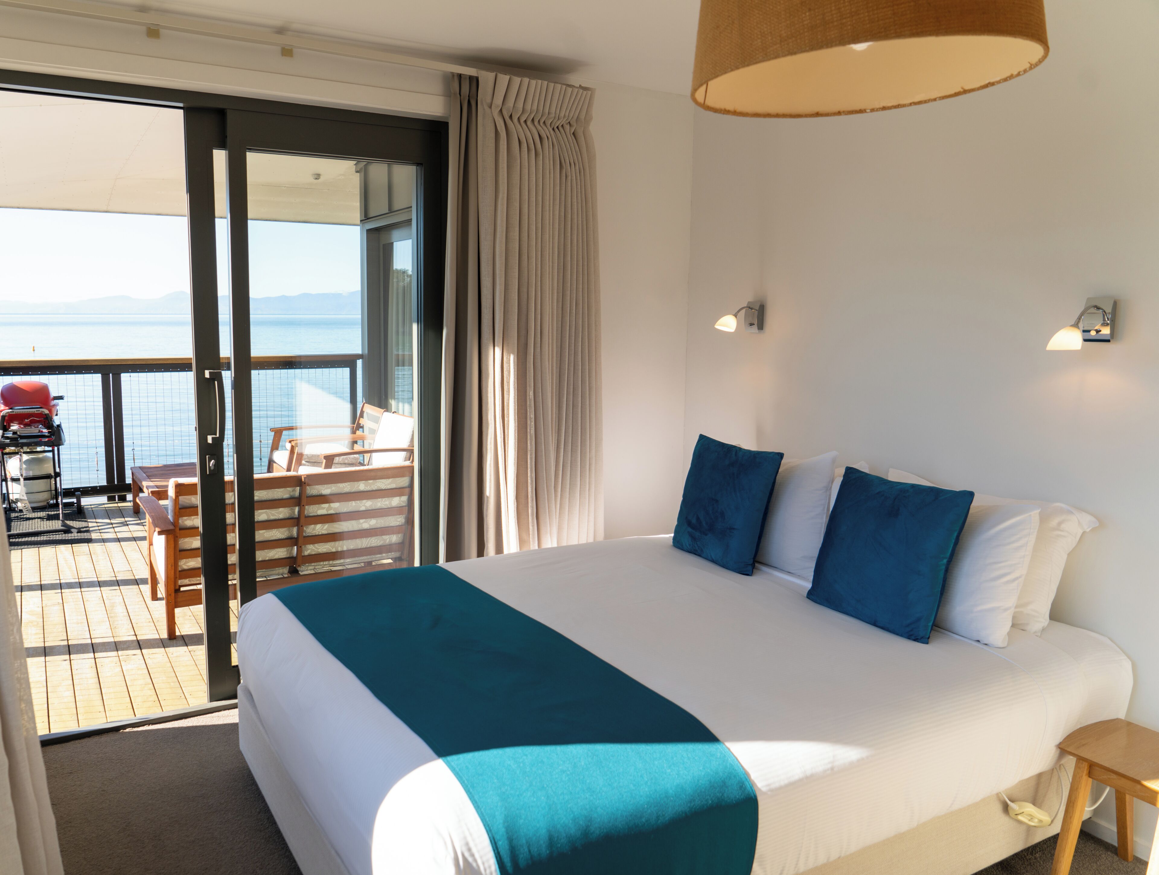 A hotel room with a large bed, a balcony with a table and chairs, and a view of the sea.