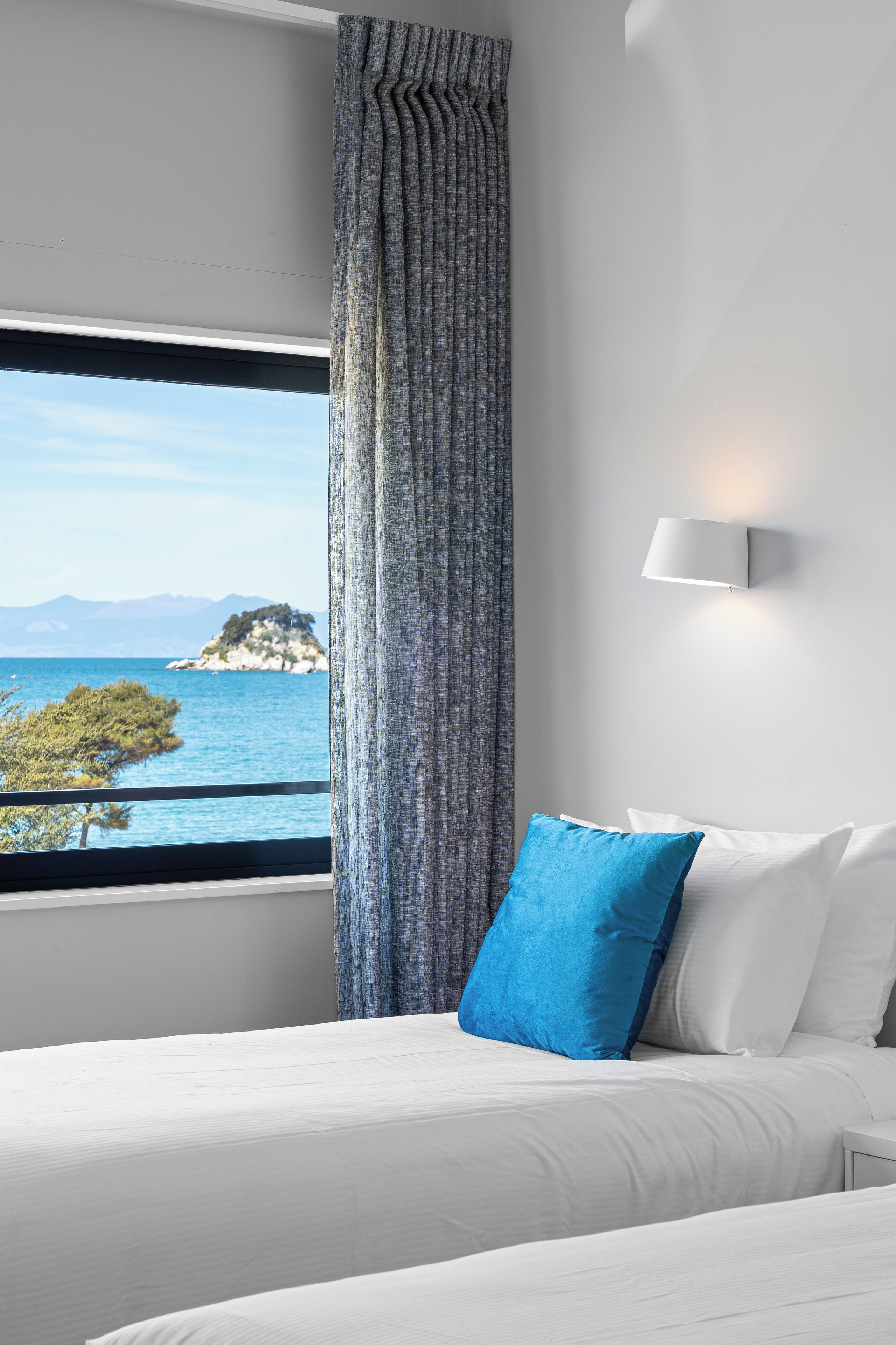 Una camera d'albergo con un letto, una finestra vista mare e una tenda.