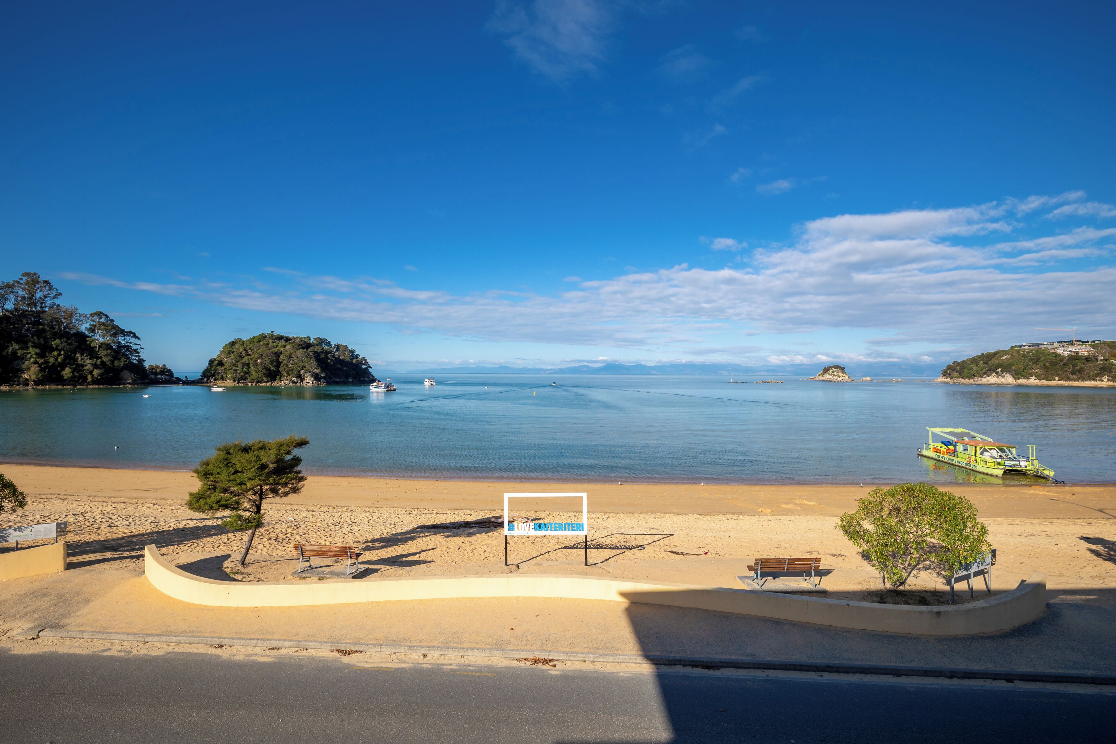 A beach with a curved walkway, benches, and a sign.