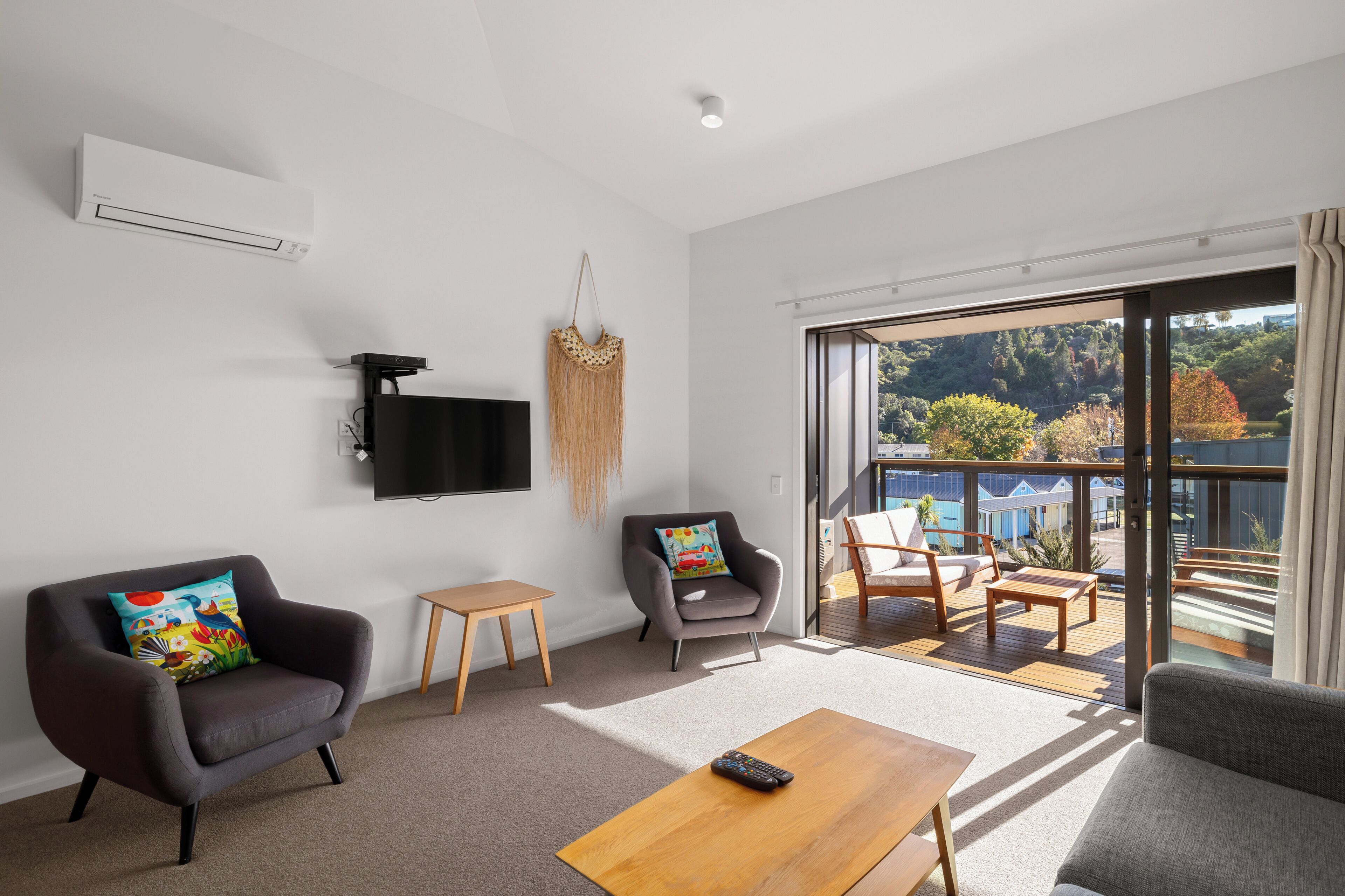 A modern living room with a flat-screen TV, two armchairs, a small table, and a balcony with a view of the city.