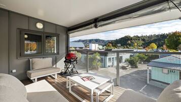 A balcony with a white table, a red grill, and a view of a mountainous landscape.