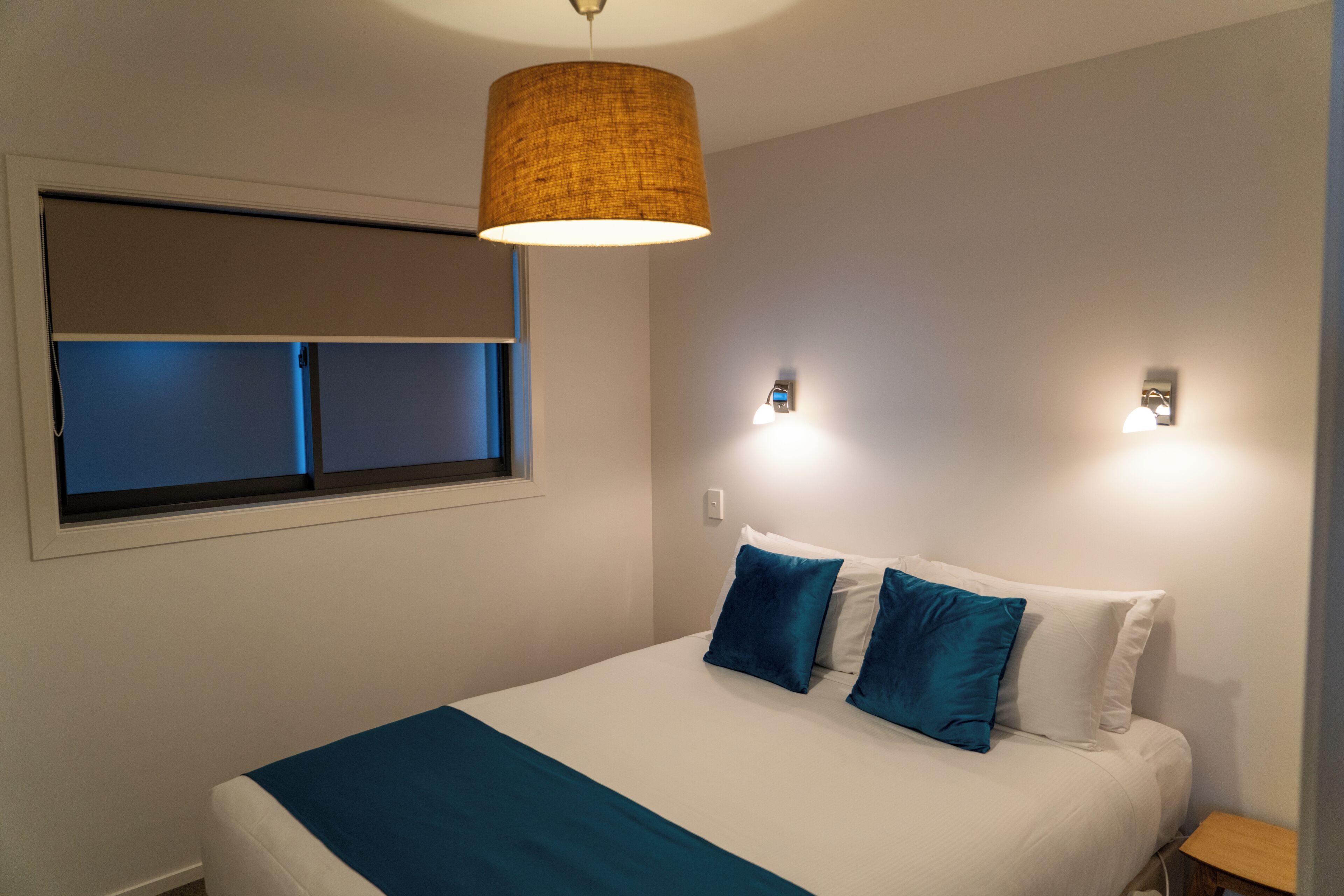 Une chambre à coucher avec un lit, une fenêtre avec des stores, un luminaire fixé au mur et un plafonnier.
