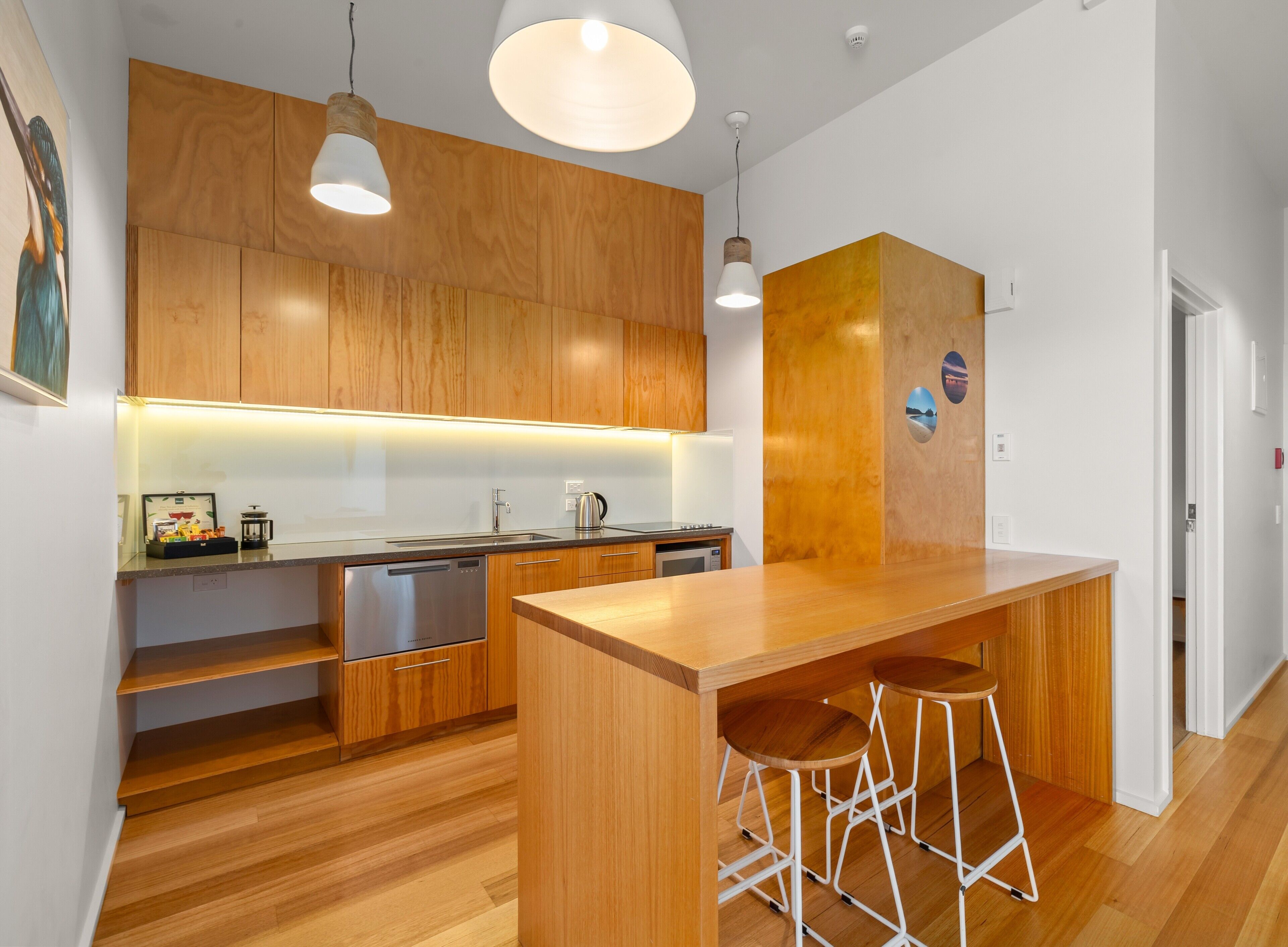 Una cocina moderna con armarios de madera, lavavajillas integrado, una isla grande con taburetes y luces colgantes, con vista al pasillo.