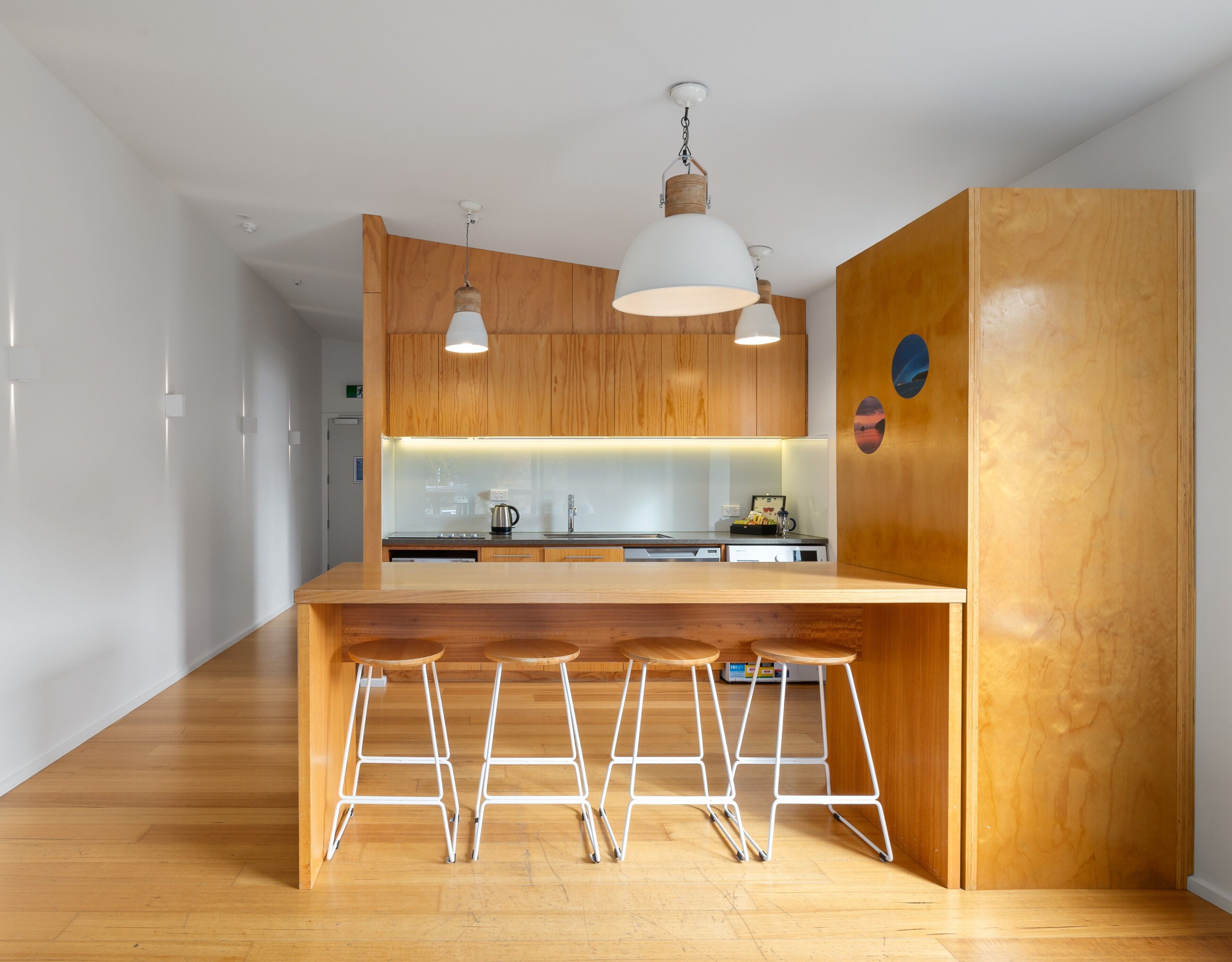 Una cocina moderna con armarios de madera, una isla central con taburetes, iluminación colgante y horno empotrado.
