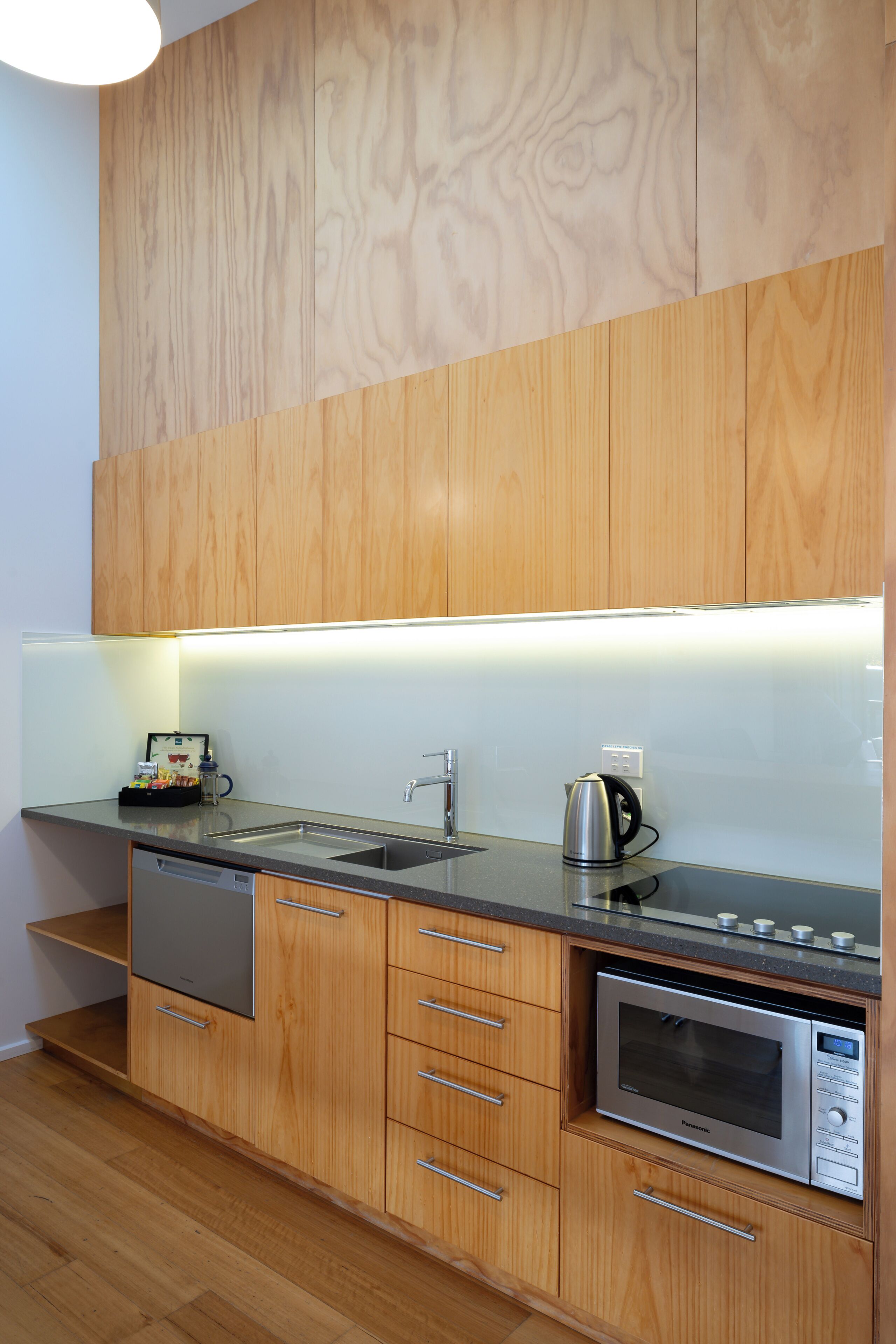 A modern kitchen with wooden cabinets, a stainless steel sink, a kettle, and a built-in microwave.