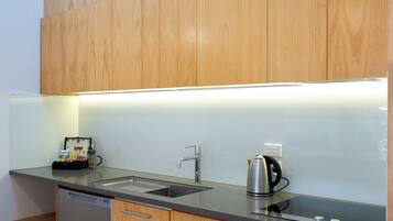 A modern kitchen with wooden cabinets, a stainless steel sink, a kettle, and a built-in microwave.