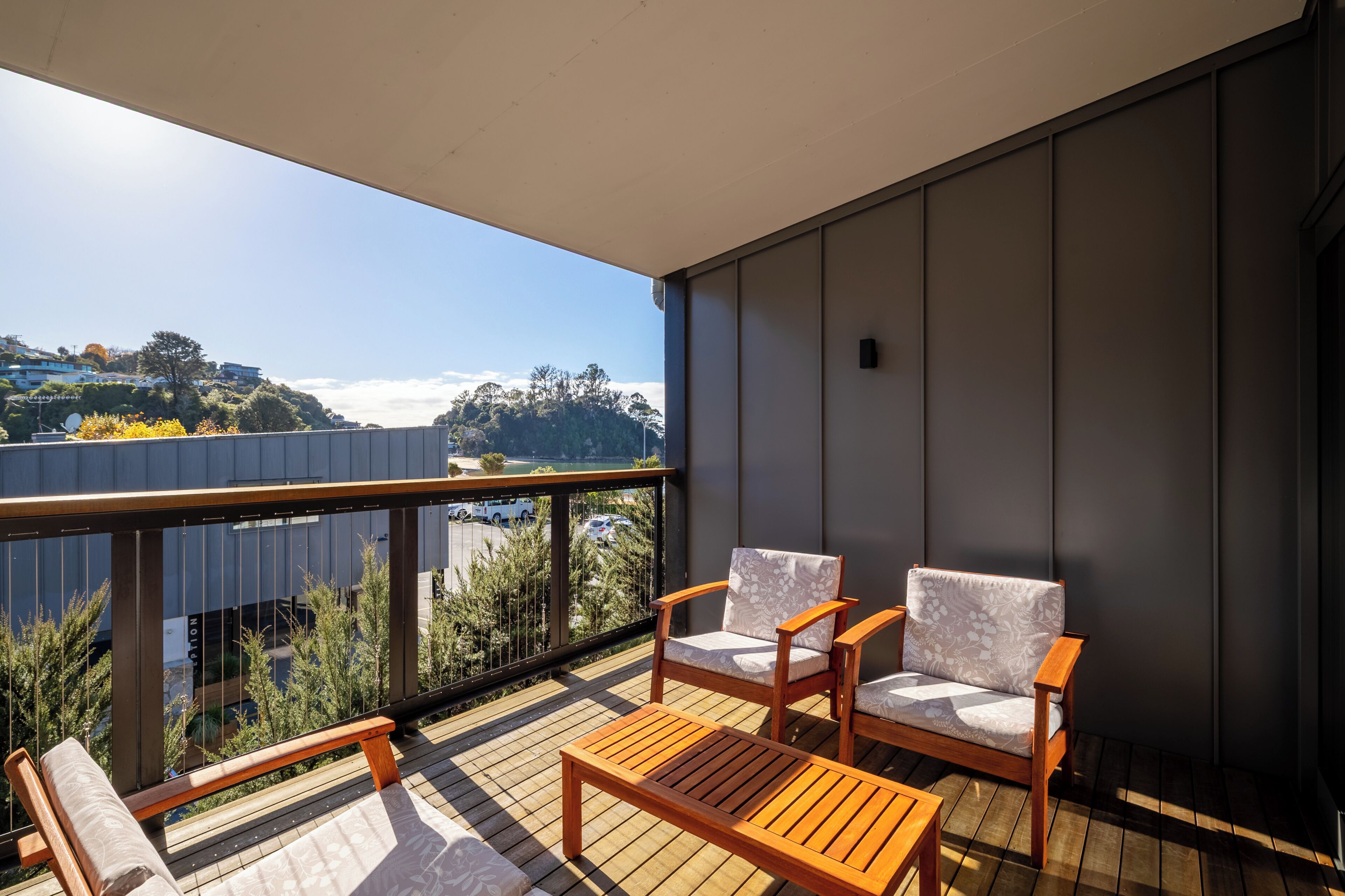 Un balcón con mobiliario de madera, vista a un paisaje urbano y cielo despejado.