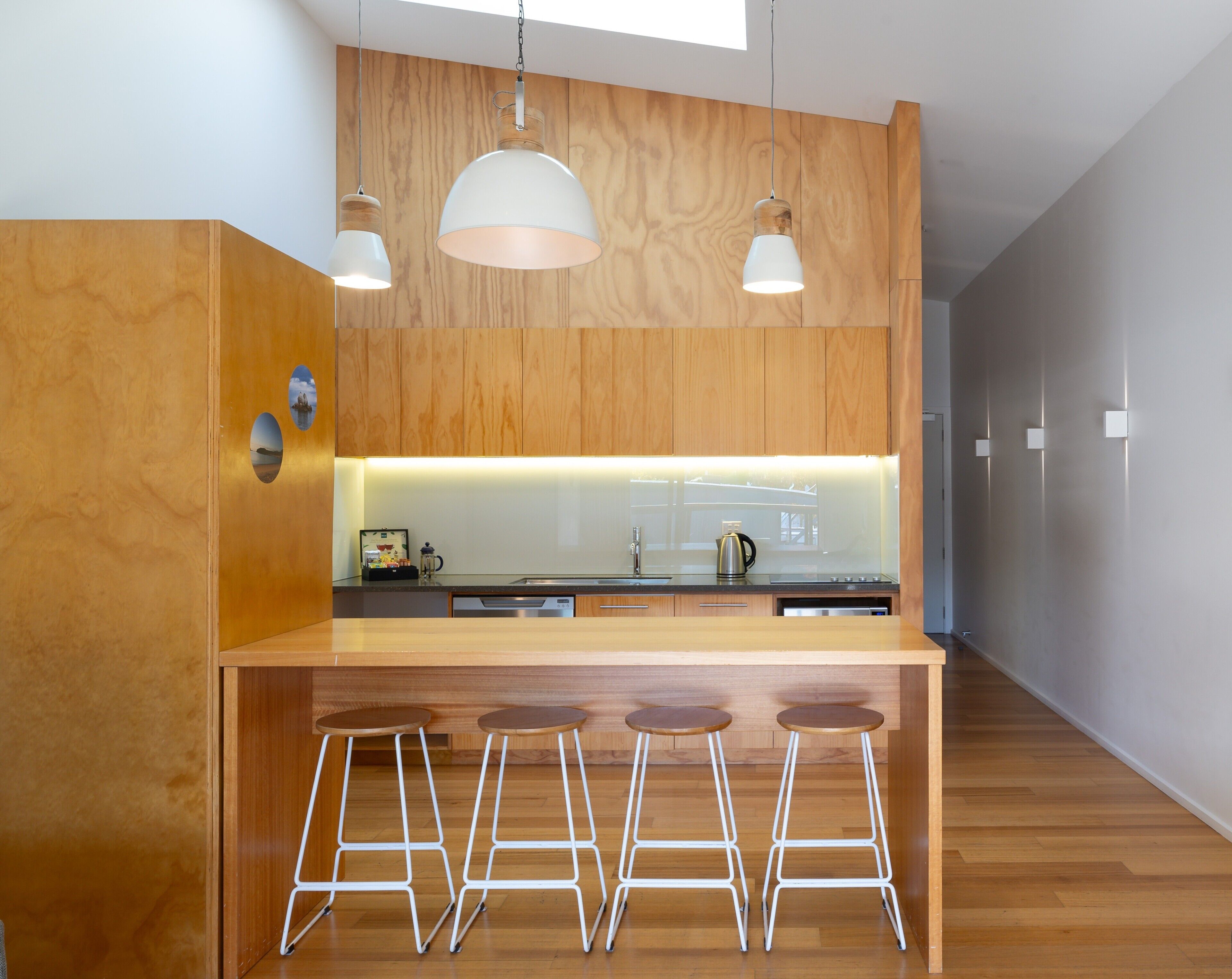 A modern kitchen with wooden cabinets, a central island with stools, pendant lighting, and a view of the adjacent room.