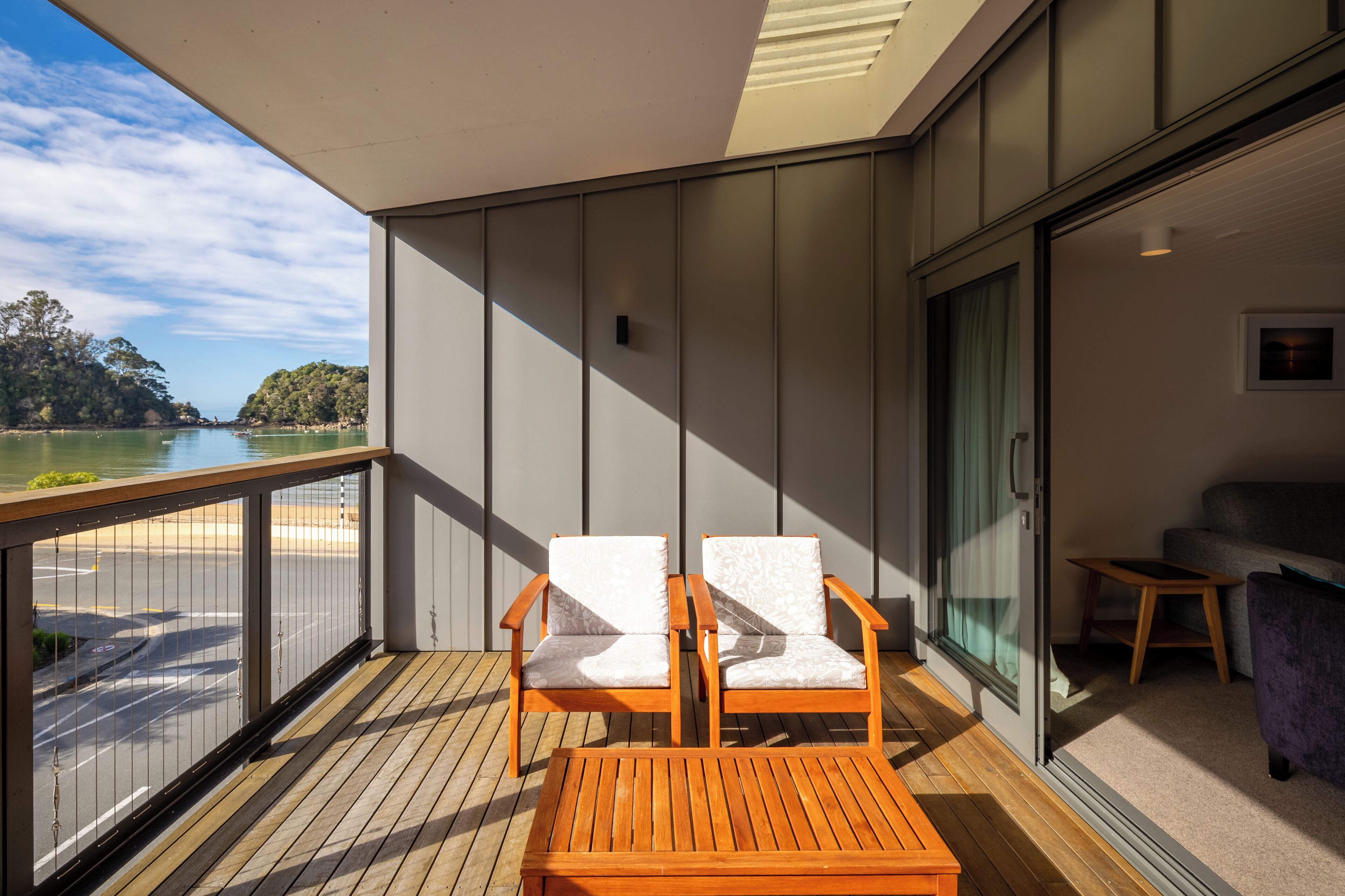 Un balcone con due sedie e un tavolo in legno, vista sulla spiaggia e sul mare.