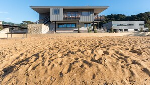 A modern two-story house with a balcony, located on a sandy beach with a clear sky. - Kaiteriteri Reserve Apartments (Kaiteriteri)