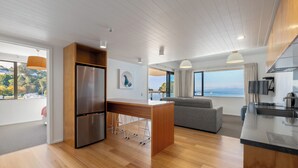 A modern kitchen with a built-in refrigerator, wooden cabinets, and a large window offering a view of the outdoors. - Kaiteriteri Reserve Apartments (Kaiteriteri)