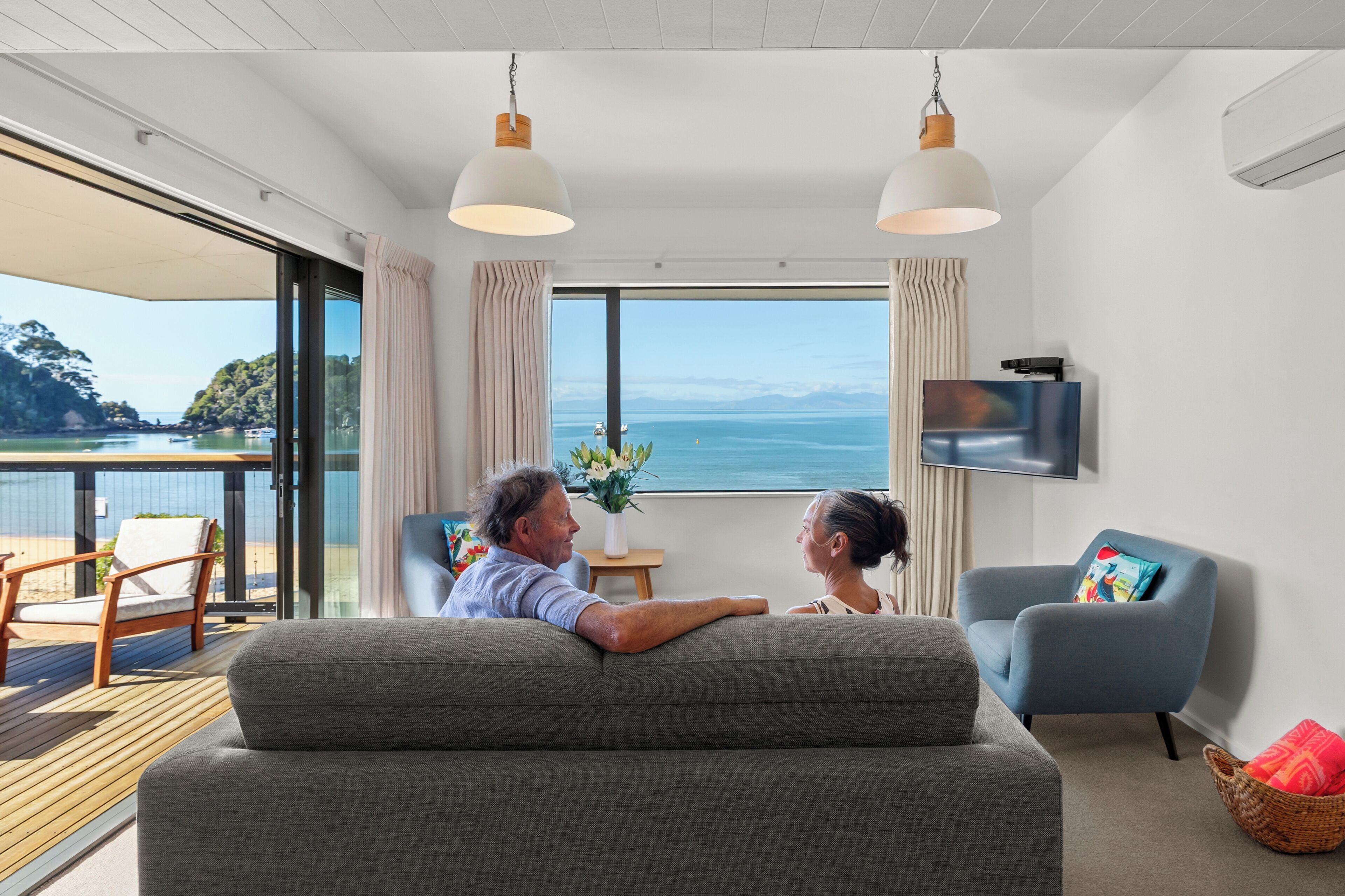 Ett modernt vardagsrum med ett stort fönster, en soffa, en tv och utsikt över havet.