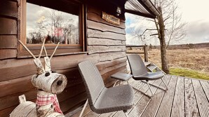 A rustic wooden cabin with a deck, two wicker chairs, and a decorative dog figure. - Cozy Forest Chalet Escape (Waimes - Sourbrodt)