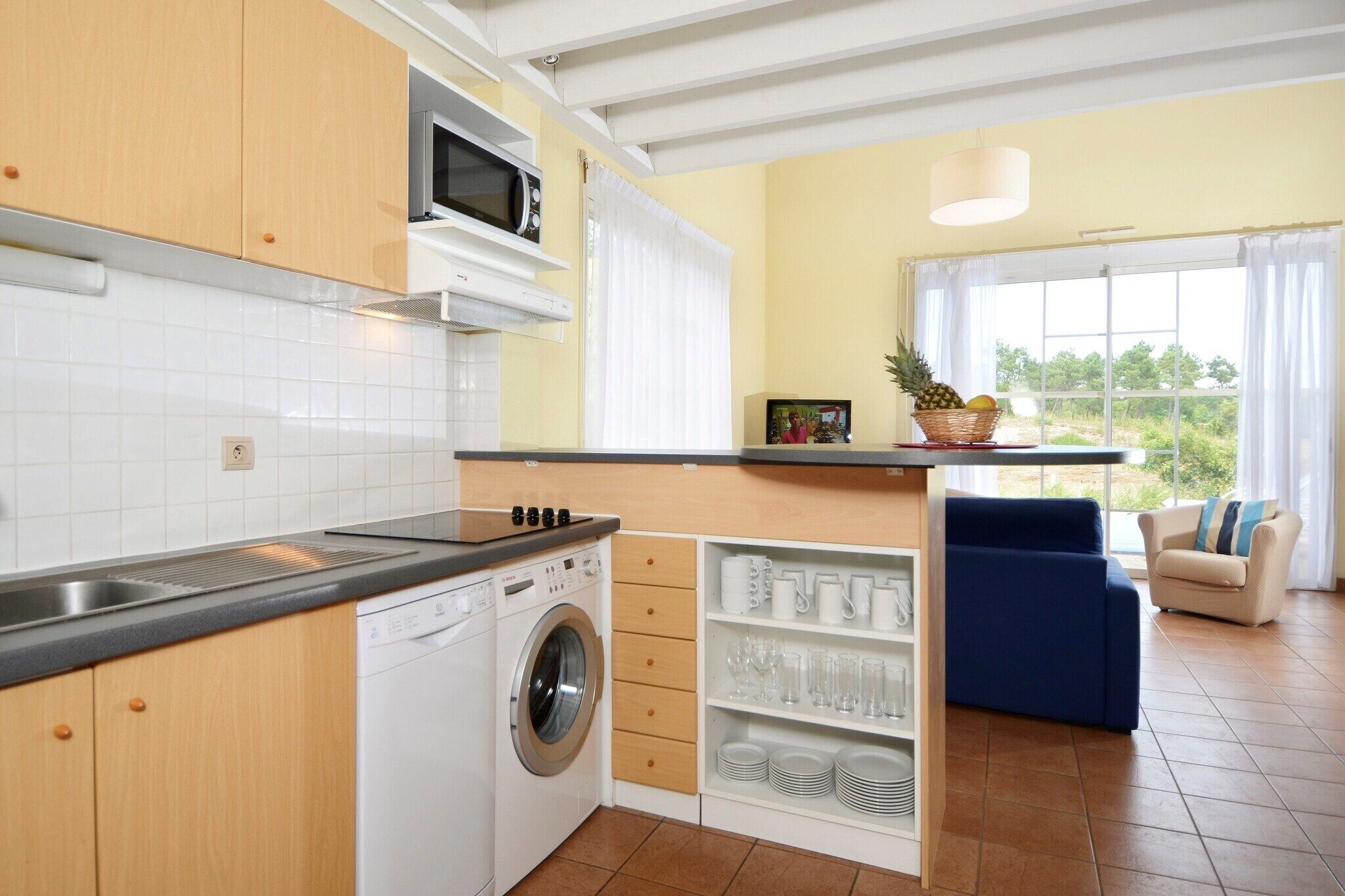 Een compacte keuken met een wasmachine, een magnetron en een eethoek met uitzicht.