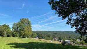 Un champ verdoyant, parsemé d’arbres, avec une vue lointaine sur des collines.