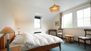 Une chambre à coucher avec un lit en bois, un bureau, une chaise, une lampe et une fenêtre avec des rideaux.