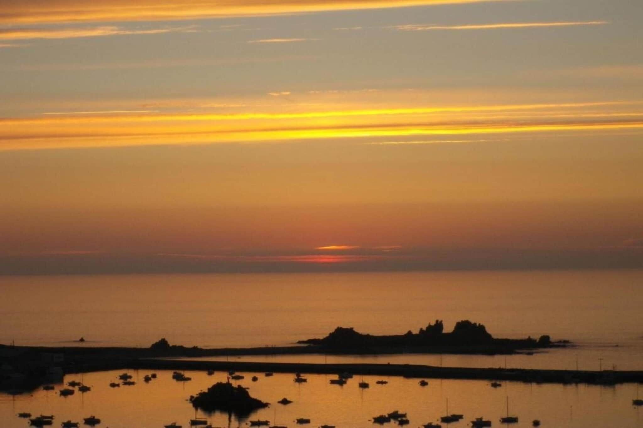 A sunset over a calm sea with boats anchored near the shore.