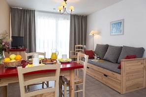 A cozy living room with a sofa, a dining table with chairs, and a television.