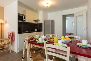 Une cuisine compacte dotée d’appareils électroménagers modernes, un coin repas aménagé pour le petit-déjeuner et une porte visible donnant sur une autre pièce.
