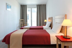Une chambre d’hôtel avec deux lits, une chaise, une table de chevet avec une lampe et une vue sur l’extérieur par une fenêtre.