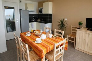 A dining area with a table set for two, a refrigerator, a microwave, and a potted plant. - Apartment in Plougasnou with Stunning Sea Views (Plougasnou)