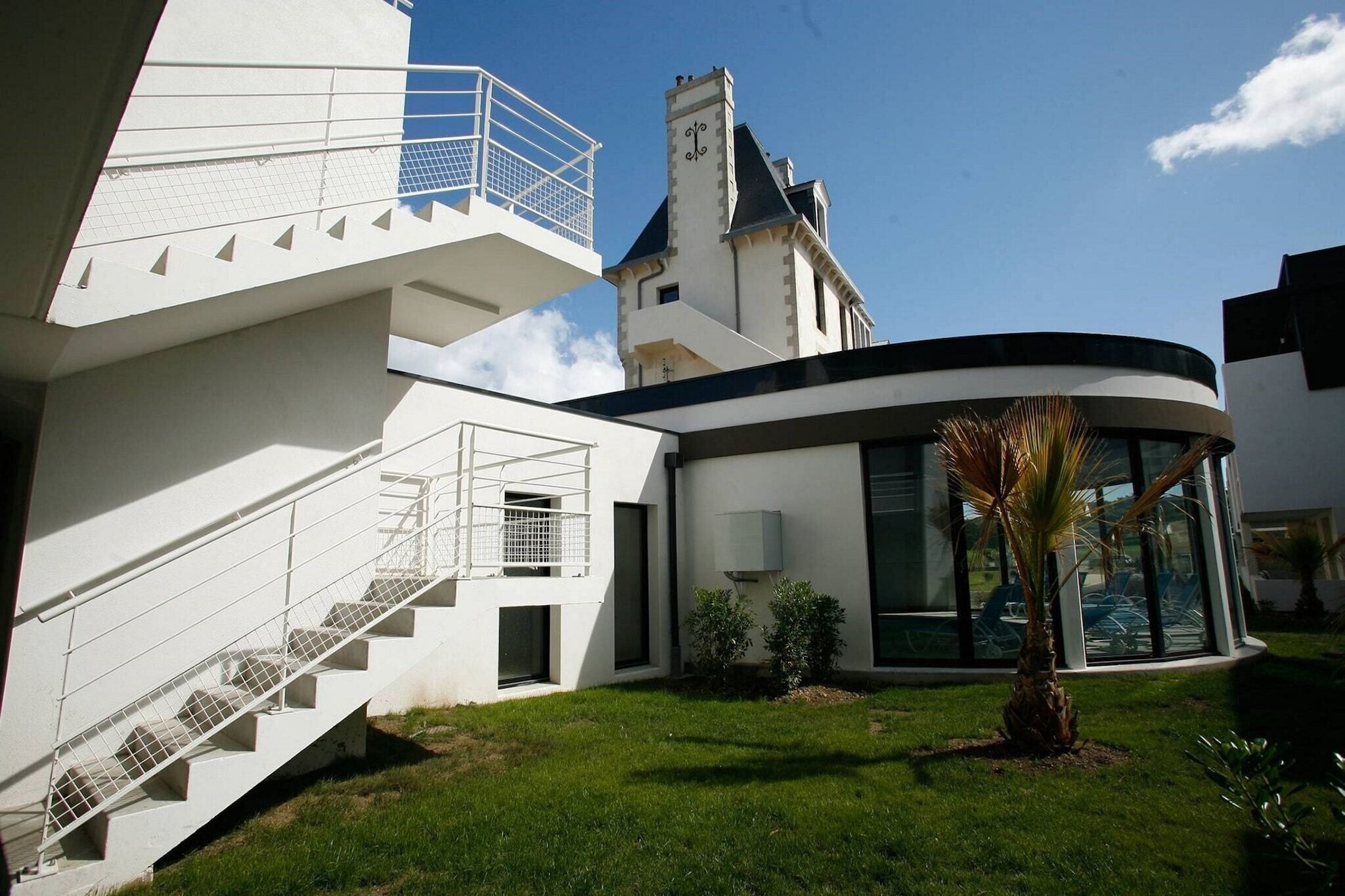 Un bâtiment moderne à l’extérieur blanc, doté d’une structure en verre incurvée et d’un escalier menant à un niveau supérieur.