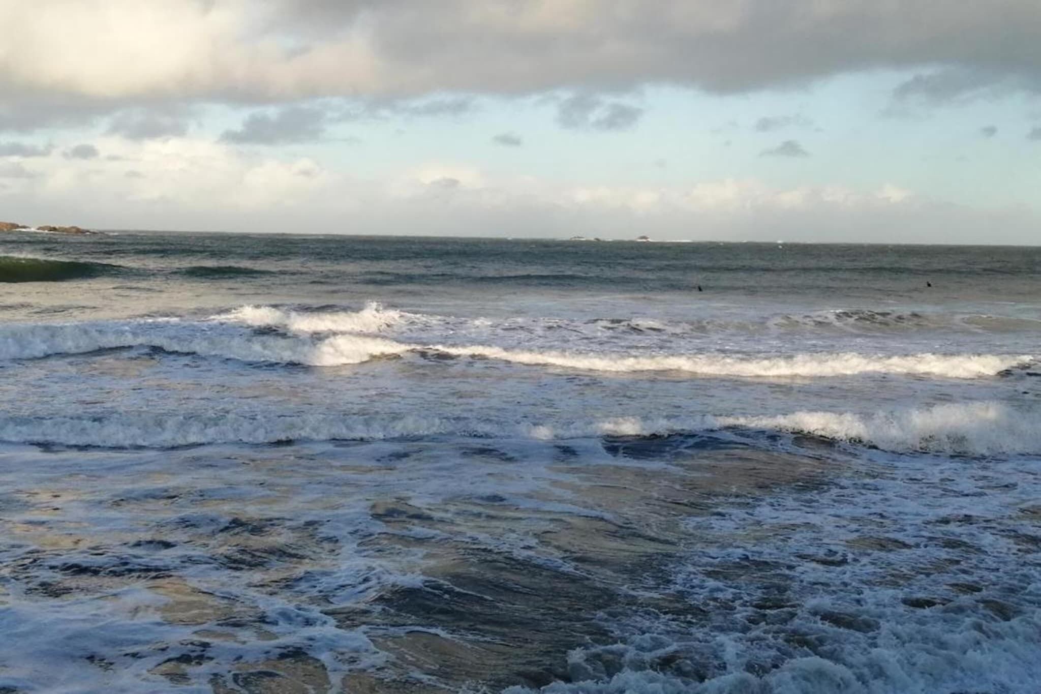 A beach with waves and a cloudy sky.