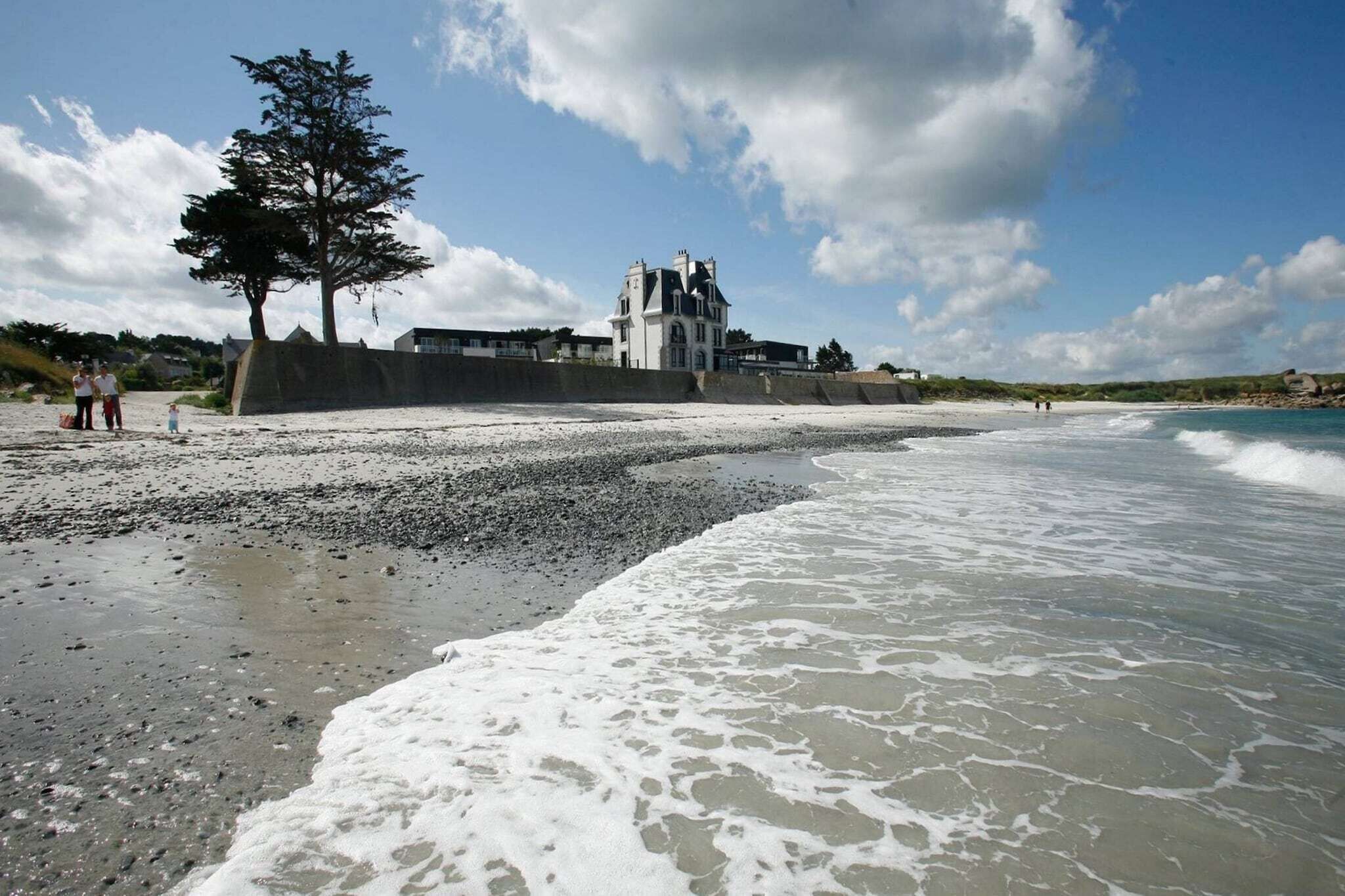 A coastal scene with a building, beach, and waves.