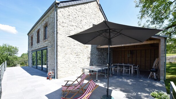 Un bâtiment en pierre doté d’un patio aménagé avec du mobilier d’extérieur, une table et un parasol.