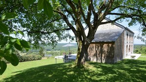 Un bâtiment rustique en pierre, doté d’un toit en pente, entouré d’une pelouse bien entretenue et d’un grand arbre qui offre de l’ombre.