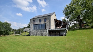 Une maison moderne en pierre, dotée d’une grande baie vitrée et d’un balcon.