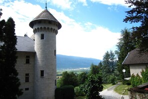 A stone tower with a conical roof, surrounded by lush greenery and a view of distant mountains. - House in France with Pool and Views (Serrieres en Chautagne)