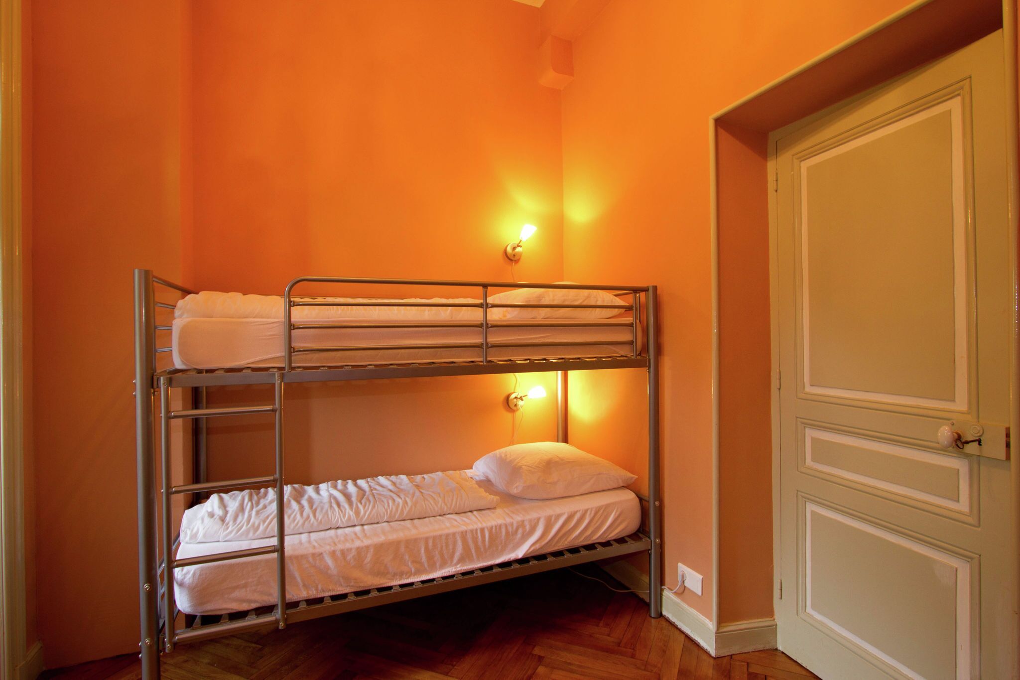 A bunk bed with two levels, a wall-mounted light, and a door with a handle.