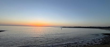 Un plan d'eau calme au coucher du soleil, avec une côte visible au loin.
