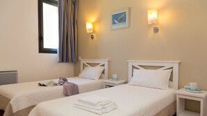 Ein Hotelzimmer mit zwei Betten, jeweils mit einem weißen Kopfende und einem Nachttisch mit Tasse und Untertasse.