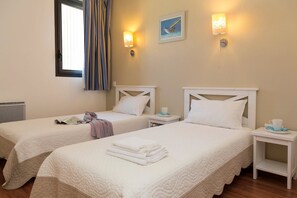 A hotel room with two beds, each with a white headboard and a bedside table with a cup and saucer. - Seaside Apartment Stay (Guidel)