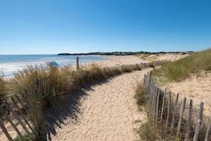 Ein Sandweg am Strand, begleitet von einem Holzzaun, der zum Meer führt.