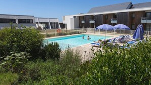 Ein Pool mit Liegestühlen und Sonnenschirmen, umgeben von Grünflächen und modernen Gebäuden.