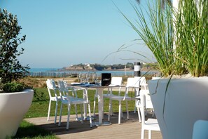 An outdoor dining area with a table and chairs, overlooking a coastal landscape. - Seaside Apartment Stay (Guidel)