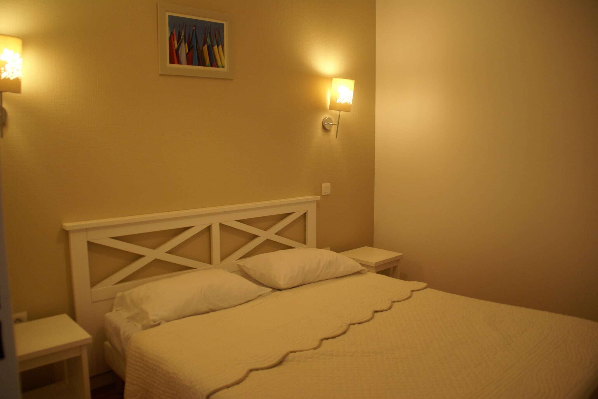 A single bed with a white headboard and two bedside tables, each with a wall-mounted light.