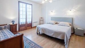 Een slaapkamer met een bed, nachtkastjes, een hanglamp, een raam met gordijnen en een kamerbreed tapijt.