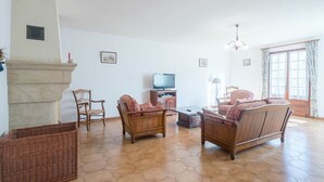Een woonkamer met een open haard, twee banken, een televisie en een groot raam met gordijnen.