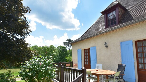 Een huis met een stenen terras, een houten tafel en blauwe luiken.