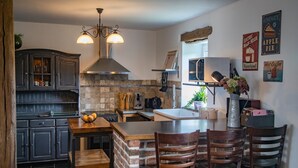 A kitchen with dark wooden cabinets, a brick island, and a dining area with four wooden chairs. - Tranquil Stay in Ardennes (Gimnée)